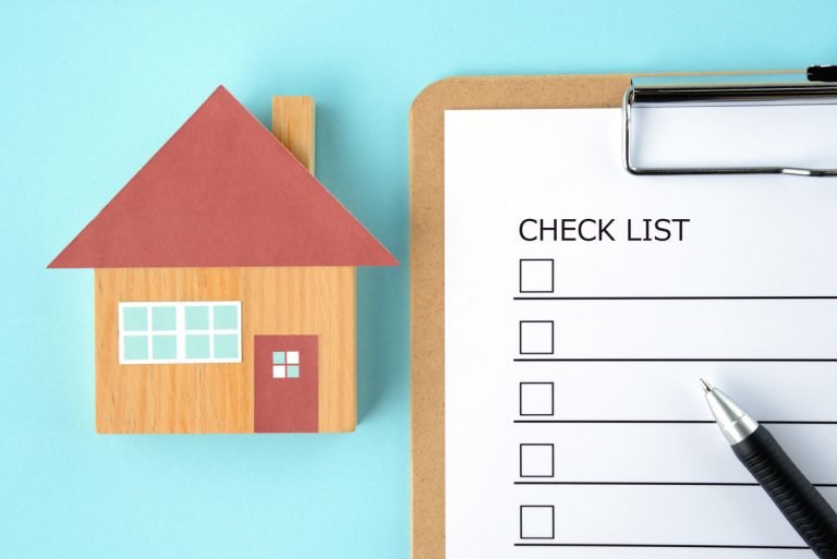 en houten speelgoedhuisje naast een klembord met een checklist en een pen. De checklist staat voor het kindveilig maken van het huis en het voorkomen van brandwonden.