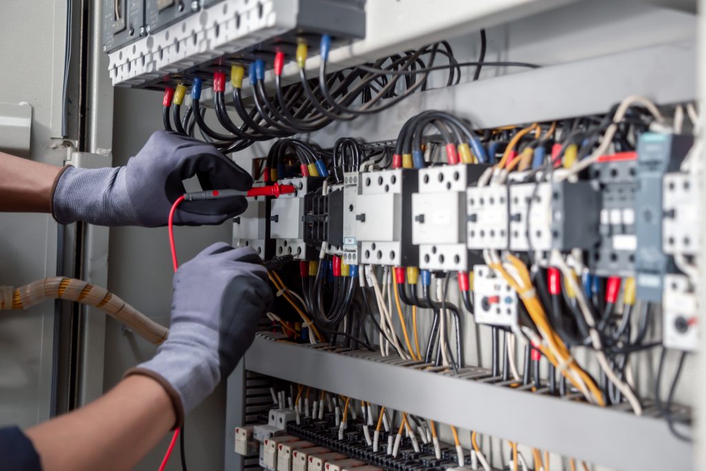 Elektricien met handschoenen voert metingen uit in een druk bedrade schakelkast